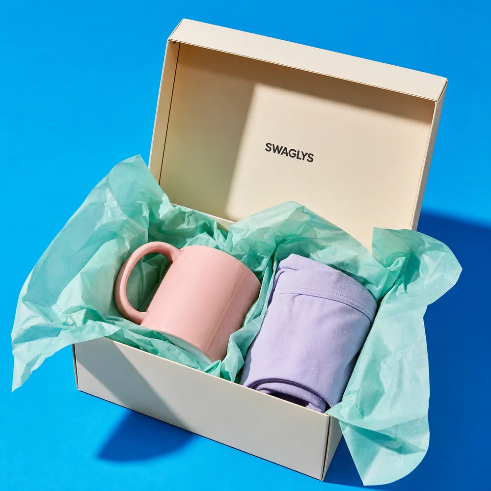 A black Swaglys gift box with lime tissue paper, a mug, and a folded tee inside